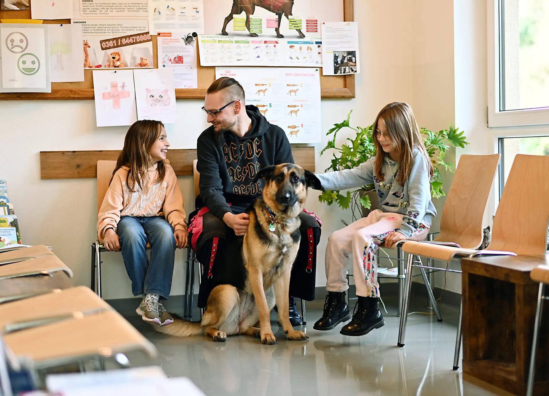 Ein Vater mit seinen zwei Töchtern und einem Hund sitzen im Wartezimmer der Praxis.